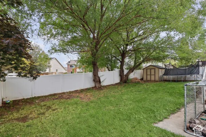 Spacious backyard featuring a white vinyl privacy fence, mature trees, and a detached storage shed