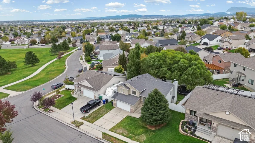 Aerial perspective of a suburban neighborhood featuring paved streets, mature trees, manicured lawns, and mountain scenery