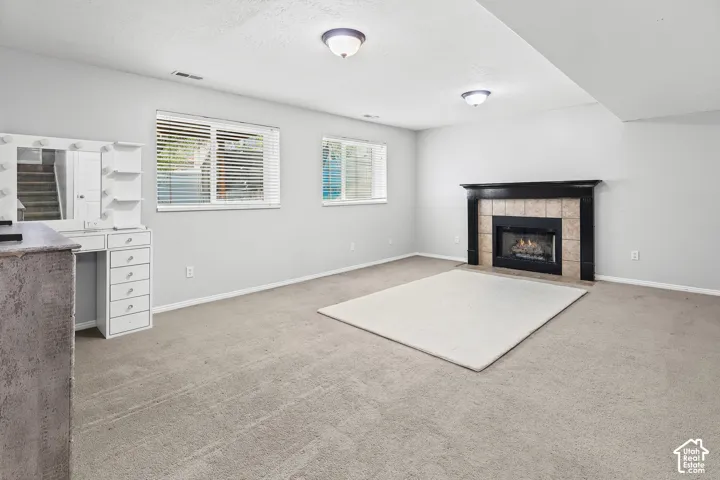 Interior space featuring carpeting, a built-in white vanity with integrated lighting, dual windows with horizontal blinds, and a fireplace with a black mantel and tile surround