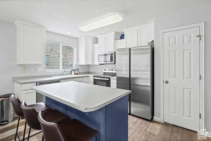 Kitchen featuring white shaker-style cabinetry, a central island with a solid surface countertop, stainless steel appliances, and wood-finish flooring