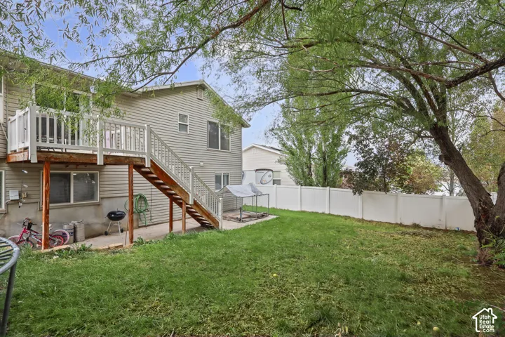 Backyard featuring a raised wooden deck with stairs, horizontal vinyl siding, white privacy fencing, and mature trees