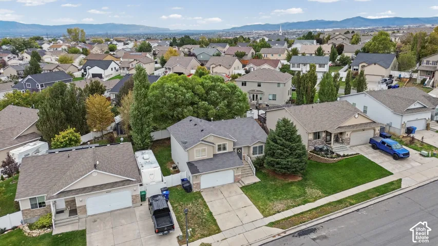 Aerial perspective of a residential suburban neighborhood featuring concrete driveways, attached garages, manicured lawns, white vinyl fencing, and a mountain range backdrop