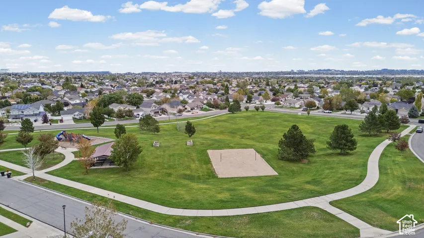 Community park featuring expansive green space, a sand volleyball court, a covered picnic pavilion, playground equipment, and paved walking paths