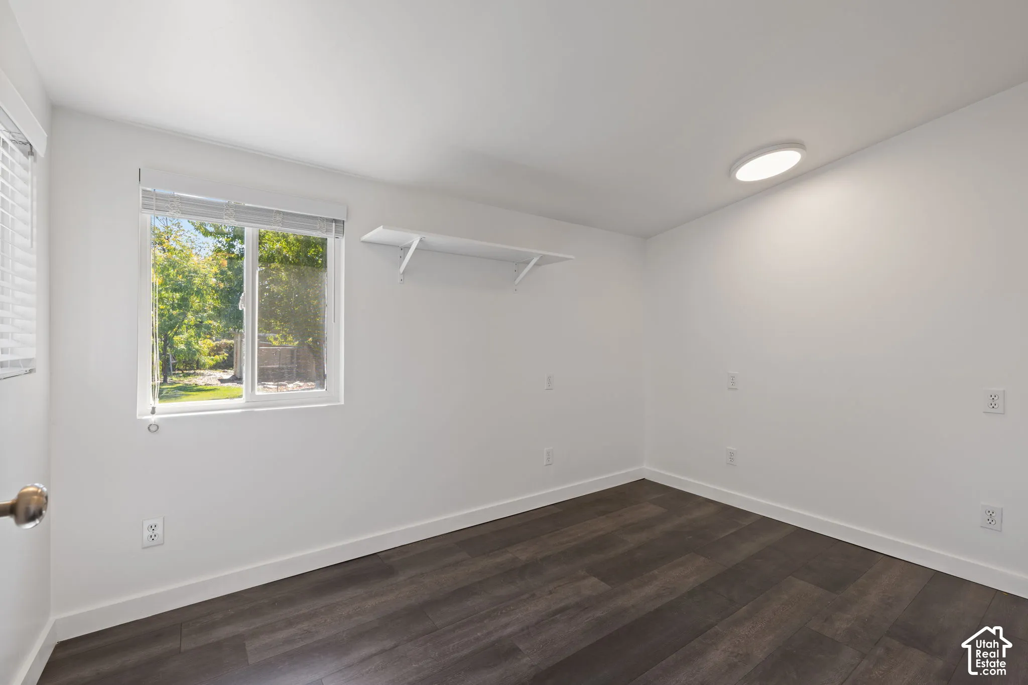 Interior room featuring wood-finish flooring, a wall-mounted floating shelf, a large horizontal window, and a flush-mount circular ceiling light