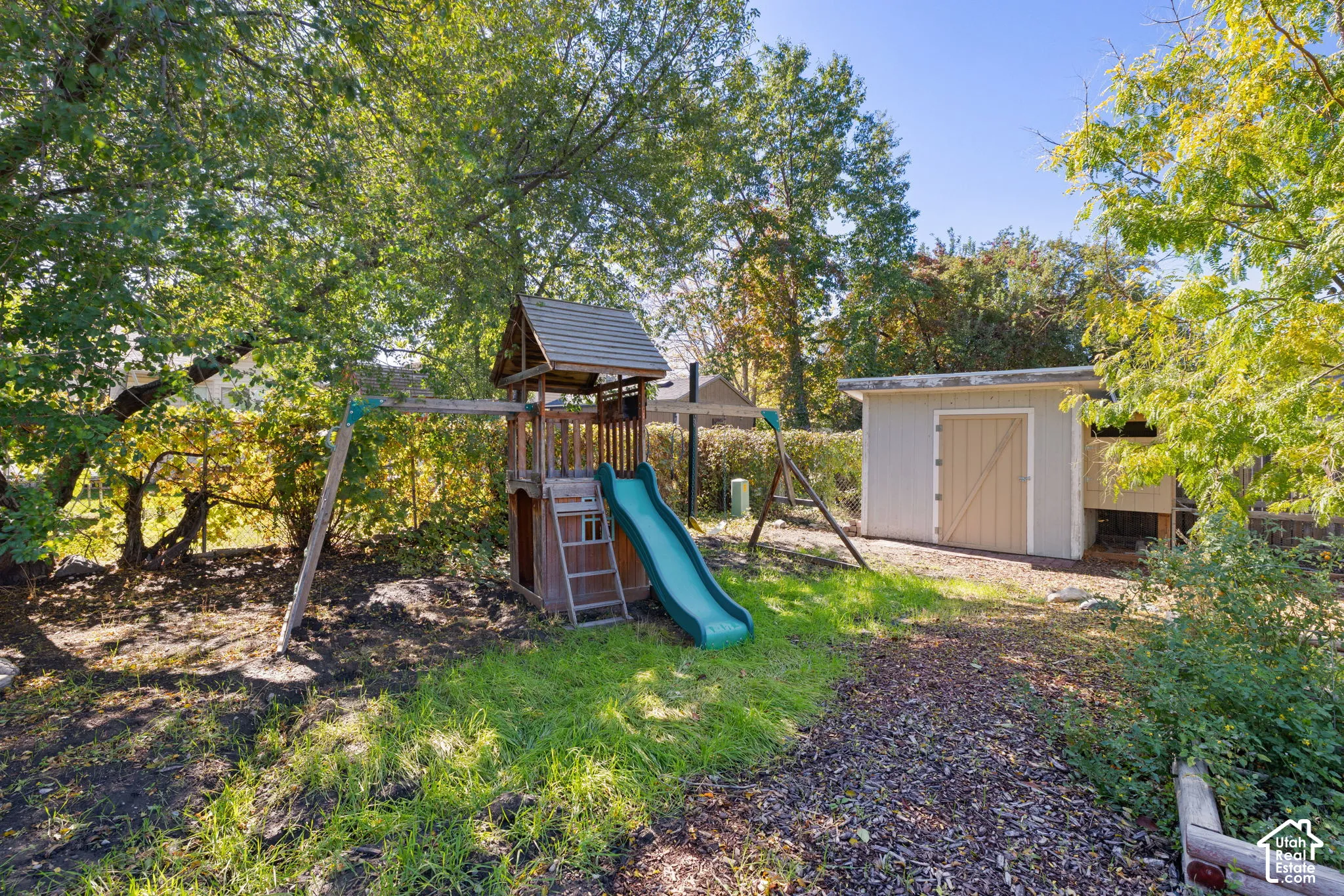 Spacious backyard featuring mature trees, a detached storage shed, and a wooden play structure with an integrated slide