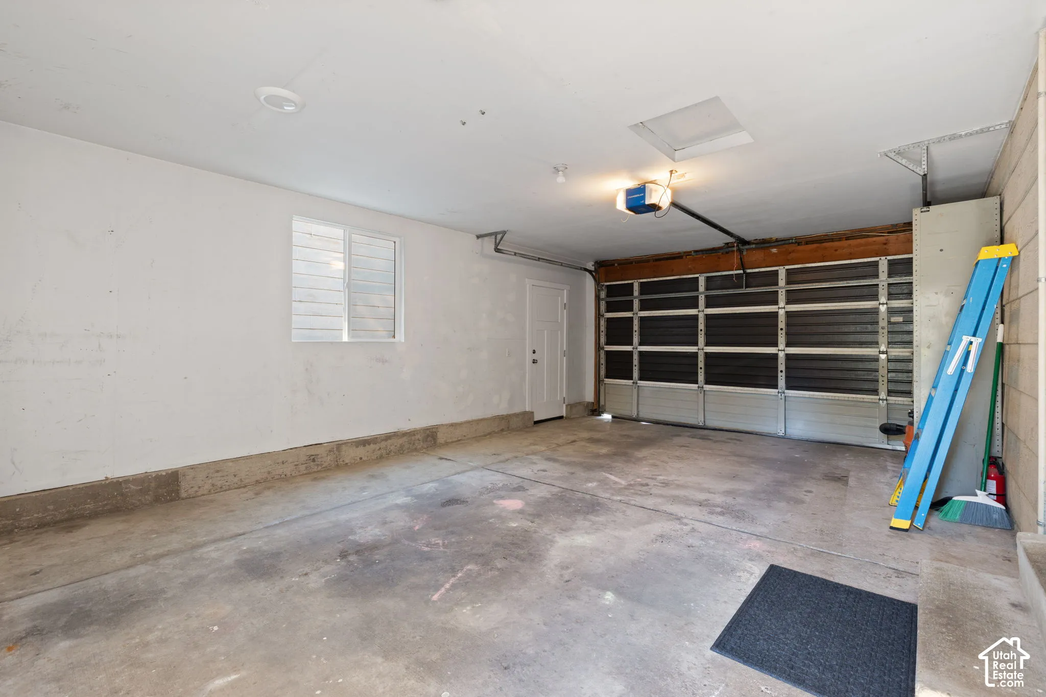 Enclosed two-car garage featuring a concrete floor, horizontal paneled garage door, integrated door opener, single-pane window, and a dedicated service door