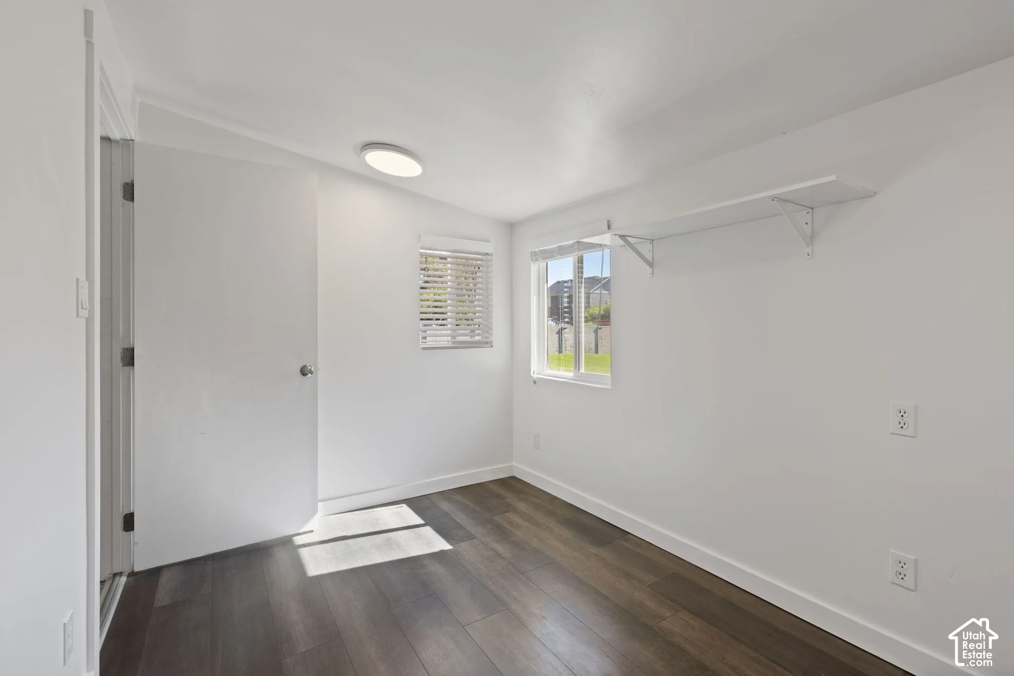 Interior space featuring wood-finish flooring, dual windows with blinds, a flush-mount ceiling light, and built-in wall shelving