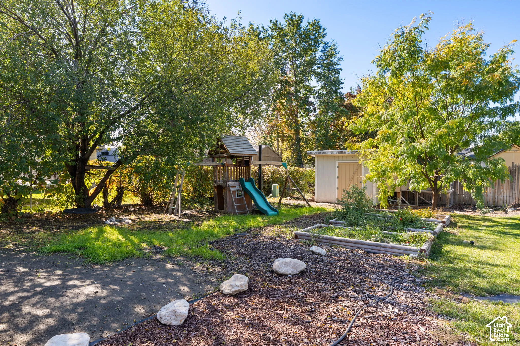 Backyard featuring mature trees, a detached storage shed, raised garden beds, and mulch landscaping
