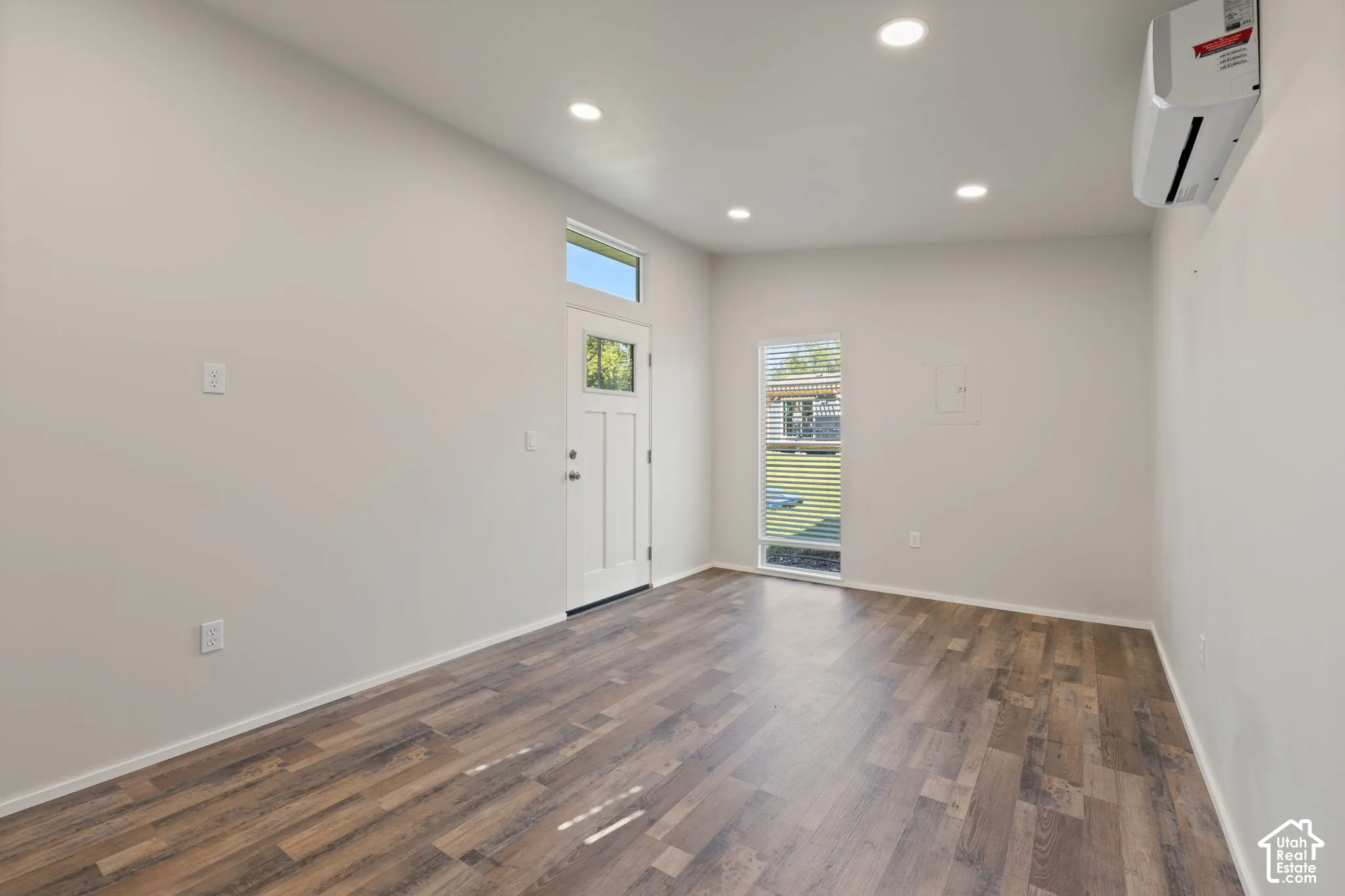 Interior space featuring wood-finish flooring, recessed lighting, a wall-mounted ductless climate control unit, and an exterior door with an integrated transom window