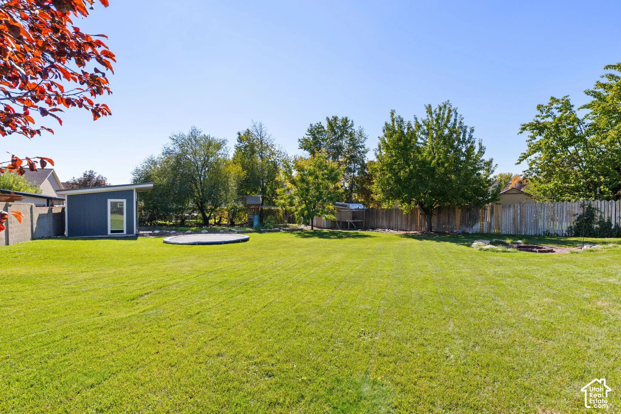 Expansive backyard featuring a manicured lawn, mature trees, wood-style privacy fencing, and a detached structure with siding