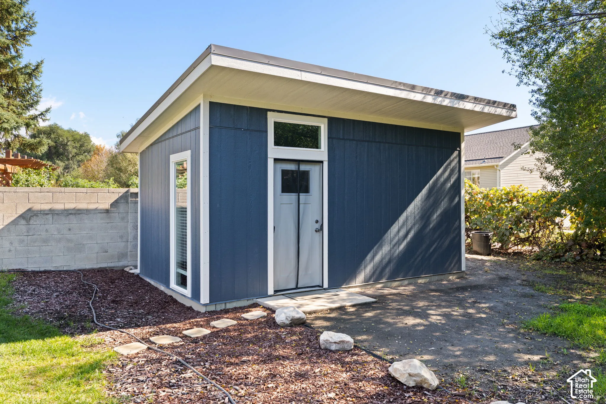 Detached outbuilding featuring vertical panel siding, a shed roofline, a transom window, and a vertical side window