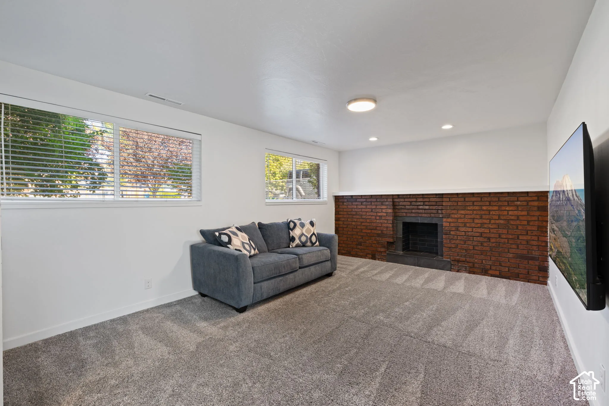 Full-wall brick fireplace featuring a flush hearth, neutral carpeting, and multiple windows providing natural light