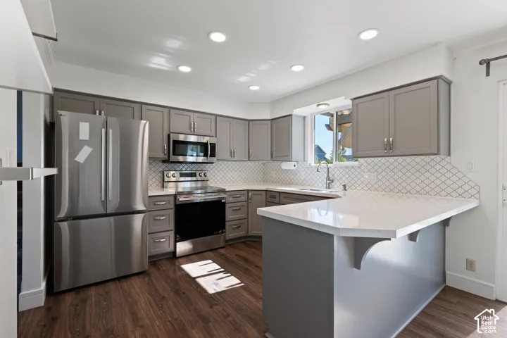 Kitchen featuring grey cabinetry, stainless steel appliances, white solid-surface countertops, patterned tile backsplash, and wood-finish flooring