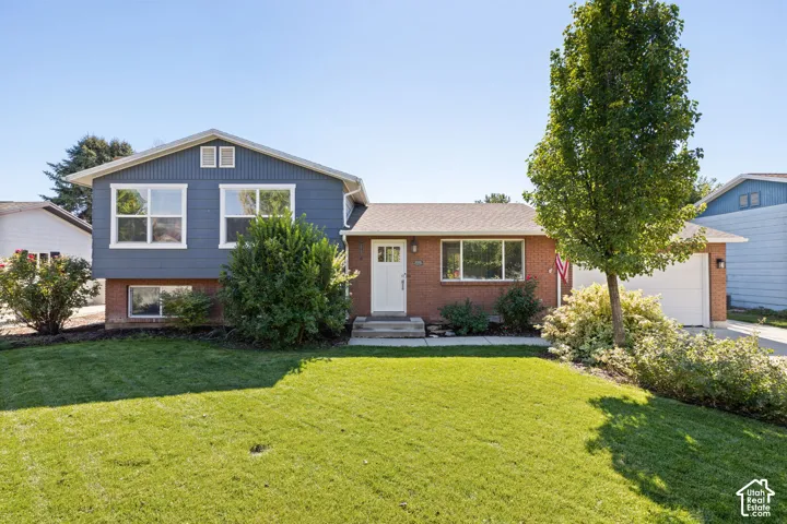 Split-level exterior featuring a combination of brick and horizontal siding, a concrete driveway, a single-car garage, and landscaped front lawn