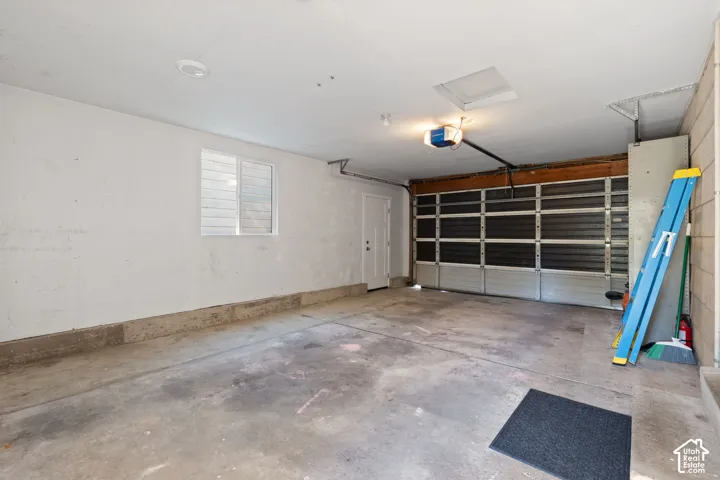 Enclosed two-car garage featuring a concrete floor, horizontal paneled garage door, integrated door opener, single-pane window, and a dedicated service door