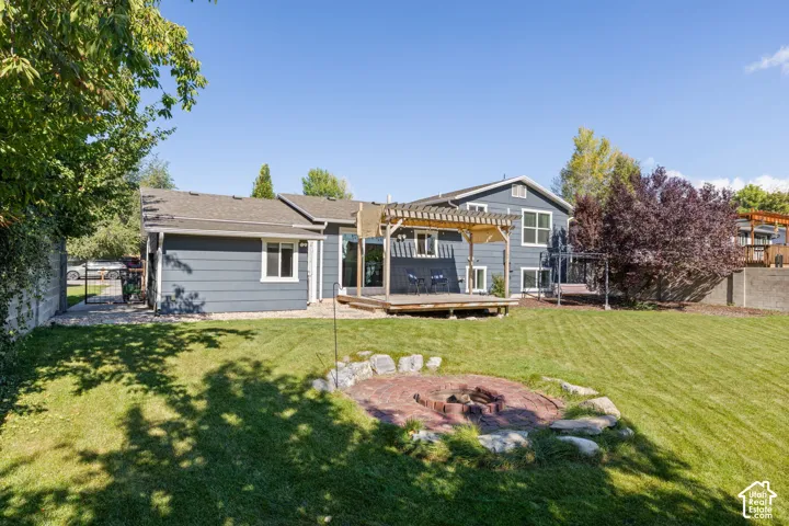 Backyard featuring a wood pergola, deck, fire pit with a stone border, and manicured lawn