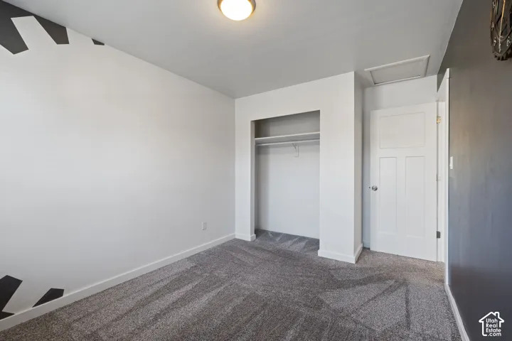 Room featuring neutral carpeting, a built-in closet with integrated shelving, a classic three-panel interior door, and a contrast wall with geometric detailing
