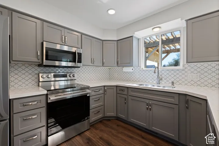 Kitchen featuring grey shaker-style cabinetry, quartz countertops, arabesque-patterned tile backsplash, stainless steel appliances, and wood-finish flooring