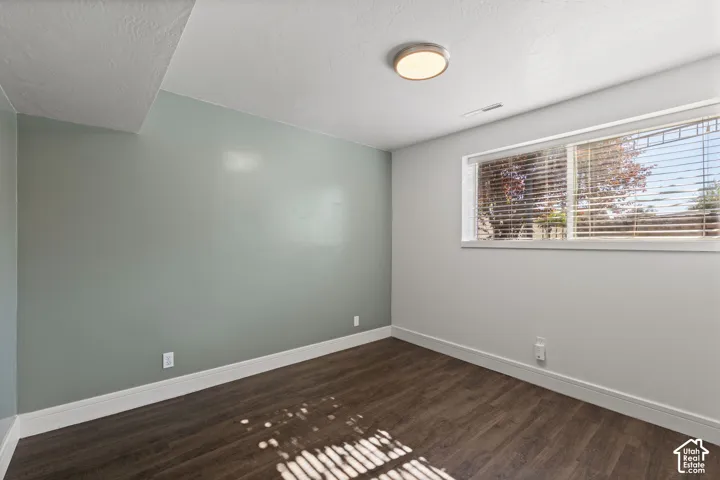 Interior room featuring wood-finish flooring, a sage green accent wall, neutral-toned walls, a large horizontal window with blinds, and a round flush-mount ceiling light