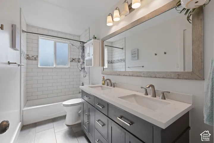 Bathroom featuring a charcoal-finished dual vanity with a white countertop, subway tile shower surround with decorative inlay, large framed mirror, and tile flooring