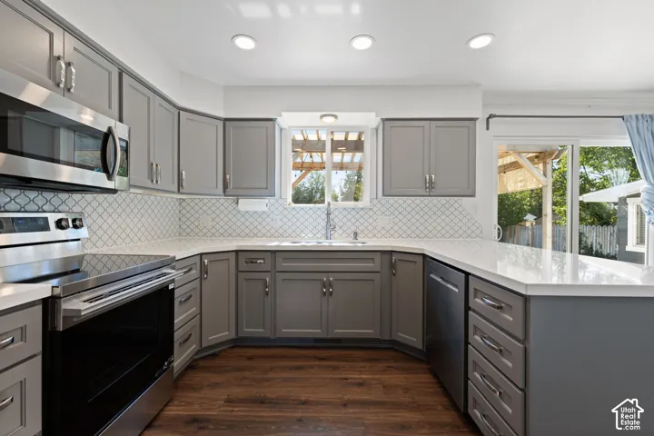Kitchen featuring grey cabinetry, white quartz countertops, stainless steel appliances, a decorative tile backsplash, and wood-finish flooring