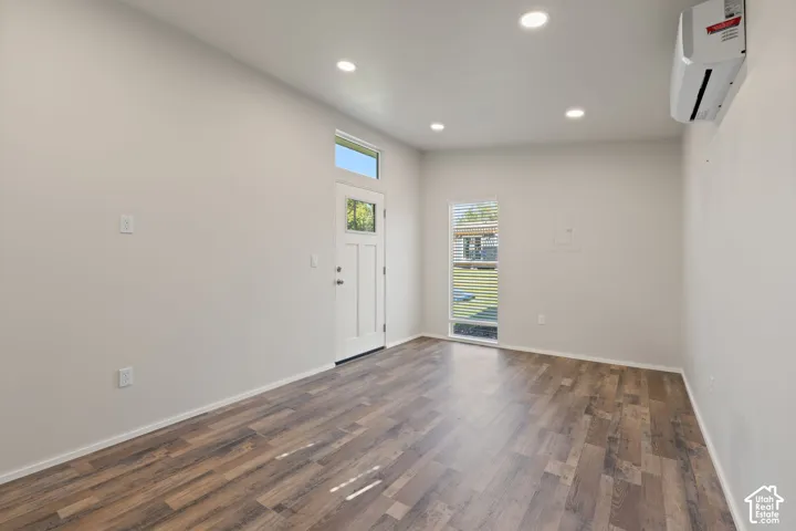 Interior space featuring wood-finish flooring, recessed lighting, a wall-mounted ductless climate control unit, and an exterior door with an integrated transom window