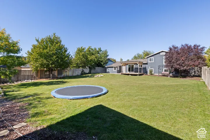 Expansive backyard featuring a large grass lawn, perimeter wooden fencing, mature trees, and a wooden deck with a built-in pergola
