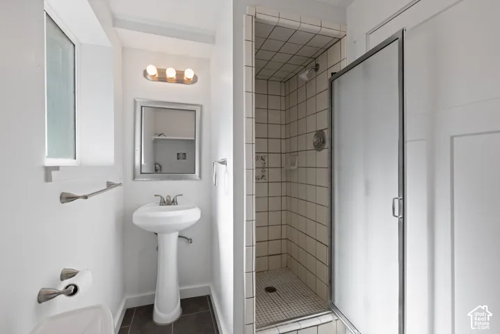 Pedestal sink with chrome-finish faucet, walk-in shower with tiled walls and glass door, and large-format tile flooring