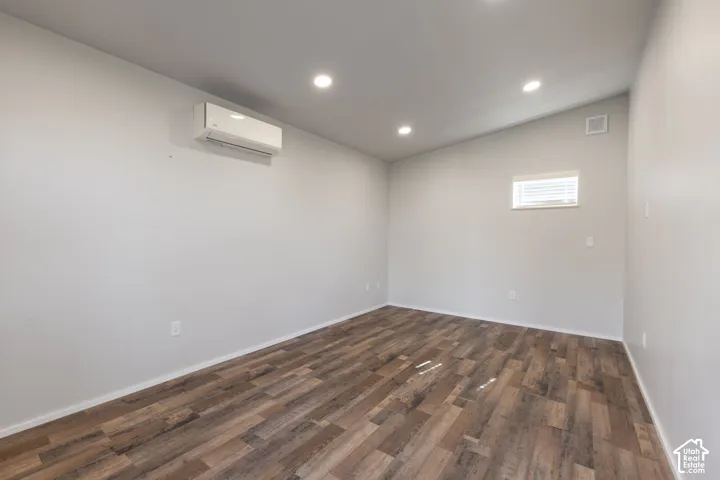 Interior room featuring wood-finish flooring, vaulted ceilings, recessed lighting, and a wall-mounted climate control unit