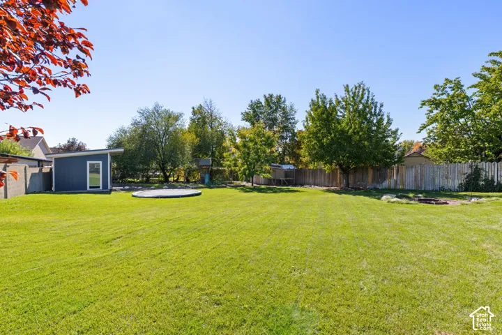 Expansive backyard featuring a manicured lawn, mature trees, wood-style privacy fencing, and a detached structure with siding