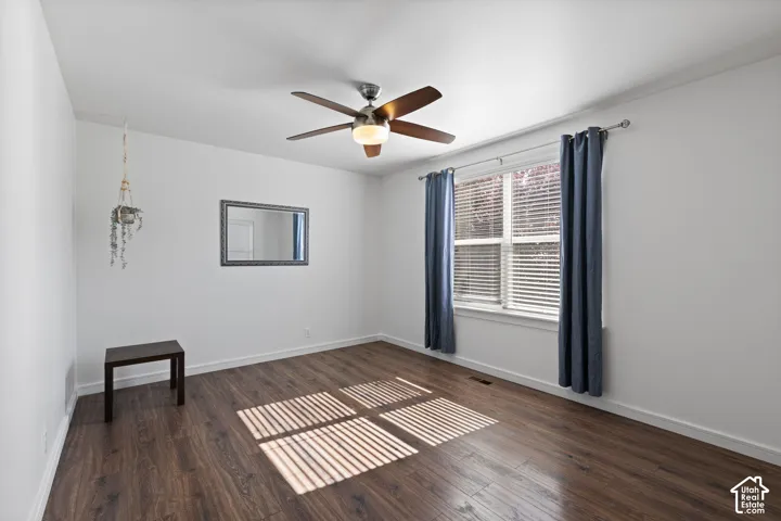 Room featuring wood-finish flooring, a multi-blade ceiling fan with integrated lighting, a window with horizontal blinds, and a fixed wall-mounted mirror
