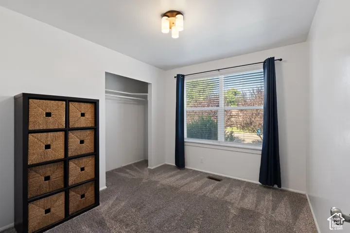 Room featuring neutral wall-to-wall carpeting, a built-in closet with overhead shelving, a multi-pane window, and a three-light flush-mount ceiling fixture