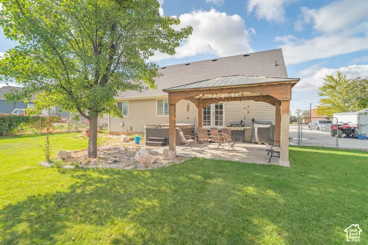Backyard featuring a wood-frame pavilion, concrete patio, mature tree, and rock garden landscaping