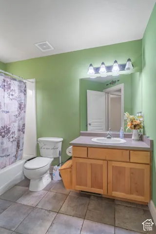 Bathroom featuring a wood-finish vanity with a molded countertop, integrated sink, four-light vanity fixture, wall-to-wall mirror, and stone-tile flooring