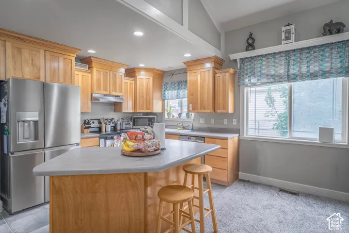 Kitchen featuring light wood cabinetry, stone-composite countertops, stainless steel refrigerator, recessed lighting, and vaulted ceilings