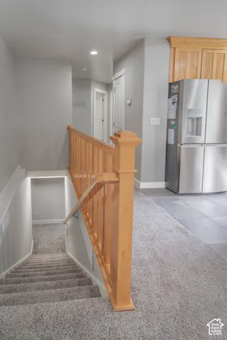 Staircase featuring natural wood handrails and balusters, carpeted treads, and stainless steel built-in kitchen cabinetry
