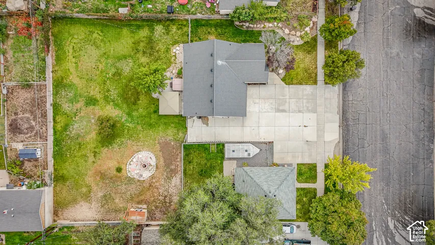 Aerial view featuring a spacious lot with a concrete driveway, multi-section backyard, stone-bordered fire pit area, and perimeter fencing