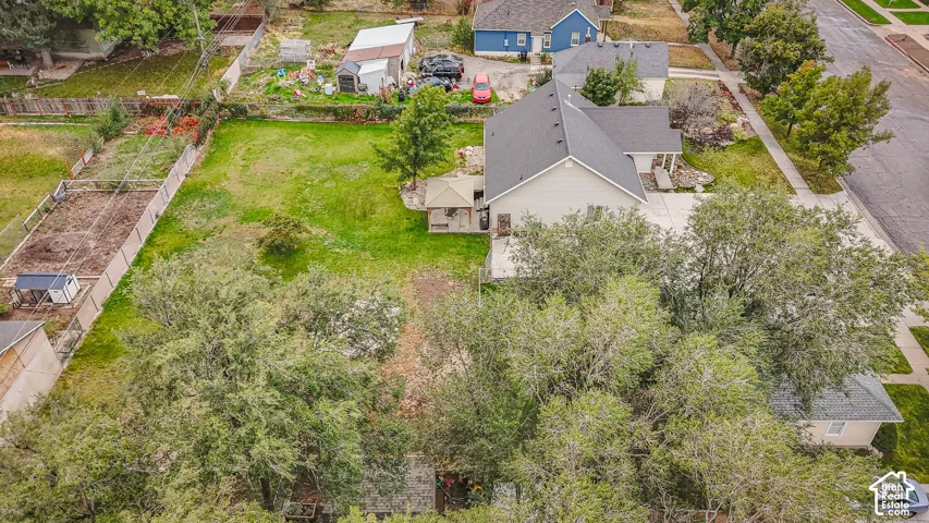 Aerial perspective of a property featuring a deep, expansive lawn, mature shade trees, a concrete driveway, and a covered patio area