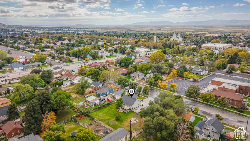 Aerial perspective of a detached residential property featuring a prominent lawn, mature trees, and a paved driveway