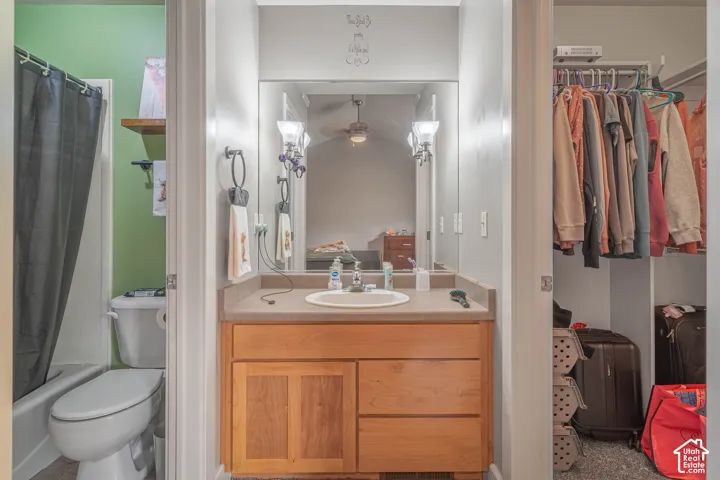 Bathroom featuring a wooden vanity with a solid-surface countertop, an oval under-mount sink, a full-width vanity mirror, dual wall-mounted light fixtures, and a walk-in closet with built-in shelving