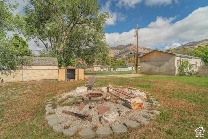 Backyard featuring a circular stone fire pit, gravel ground cover, boulder border accents, mature trees, and a mountain backdrop