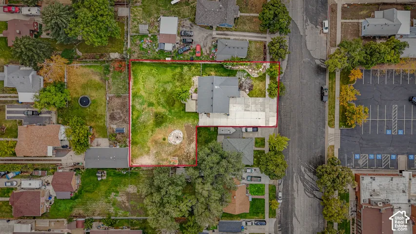 Aerial perspective of a corner lot property featuring an L-shaped parcel, a detached garage, a concrete driveway, and mature landscaping