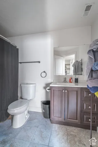 Bathroom featuring a dark wood vanity with stone-finish countertop, integrated sink, large frameless mirror, and tile flooring