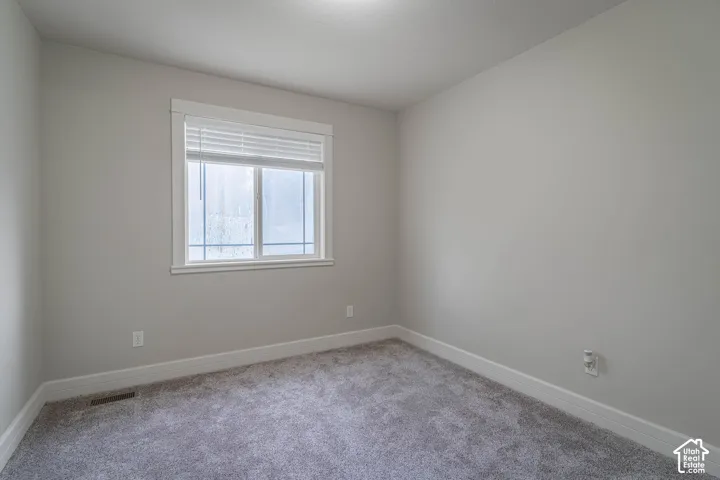 Neutral-toned interior space featuring light-colored wall paint, plush carpeting, and a multi-pane window with white trim and integrated blinds