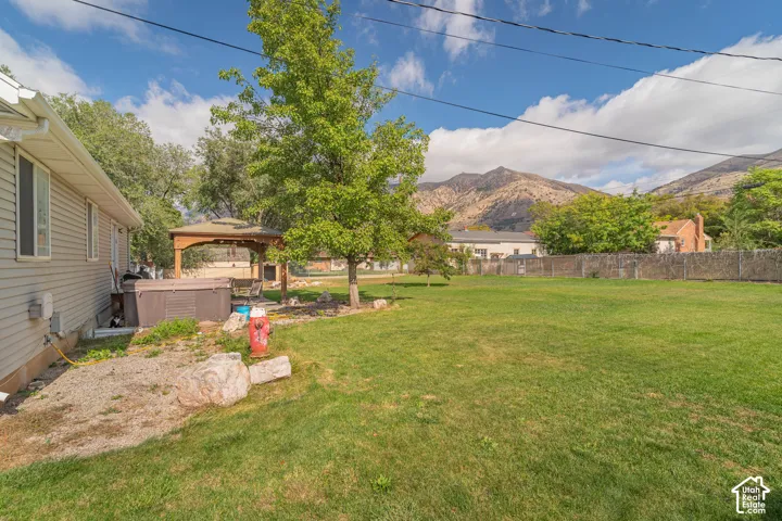 Expansive backyard featuring a grass lawn, mountain backdrop, wooden gazebo, and perimeter fencing