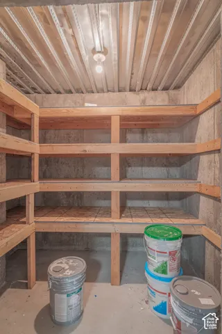 Storage area featuring multi-tier built-in wood shelving, exposed concrete walls, corrugated metal ceiling, and mounted overhead lighting