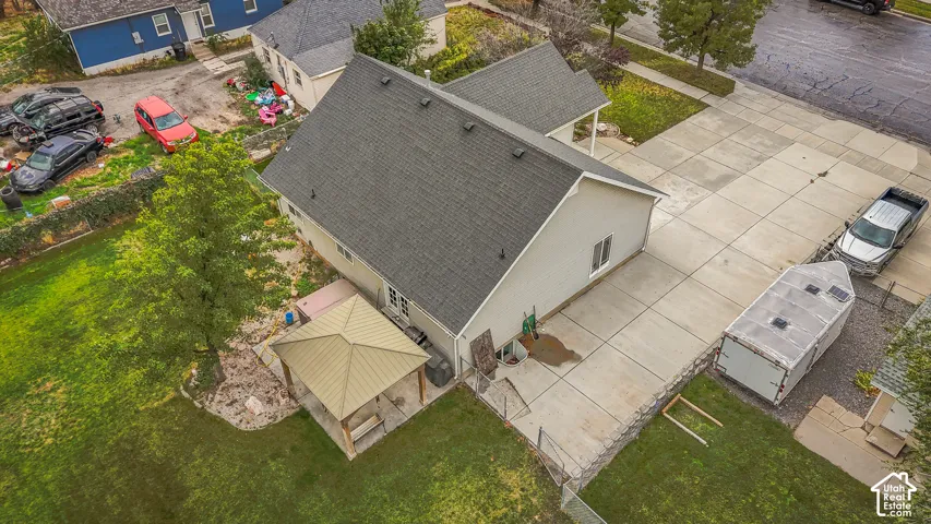 Aerial view of a property featuring a detached structure with a pitched shingle roof, a spacious concrete driveway, and an outdoor gazebo