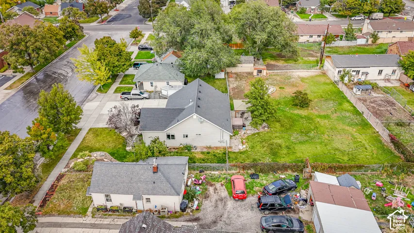 Aerial perspective of a multi-structure parcel featuring a pitched shingle roof, expansive open grounds, mature trees, and detached garage space