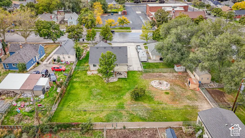 Expansive backyard featuring a large grass lawn, mature trees, stone-bordered fire pit area, concrete driveway, and covered patio