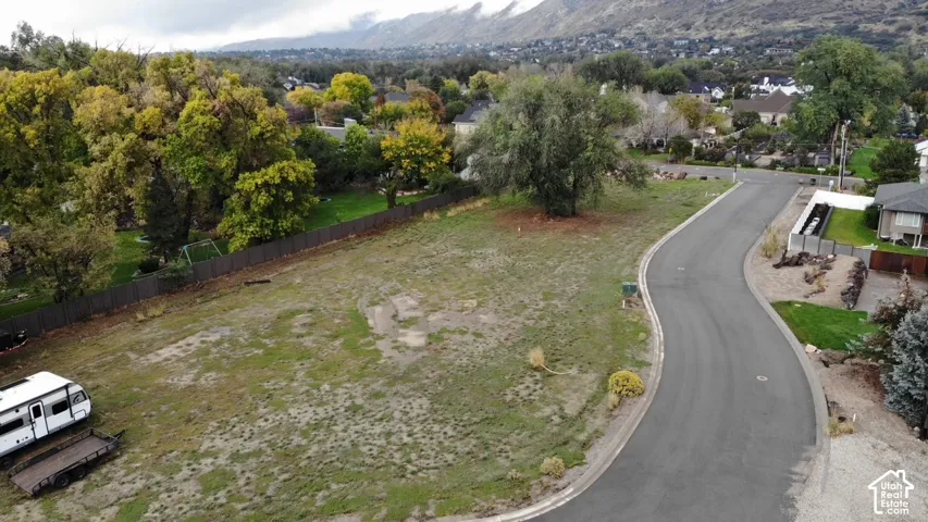 Expansive corner lot featuring asphalt street frontage, perimeter privacy fencing, mature trees, and a mountain backdrop